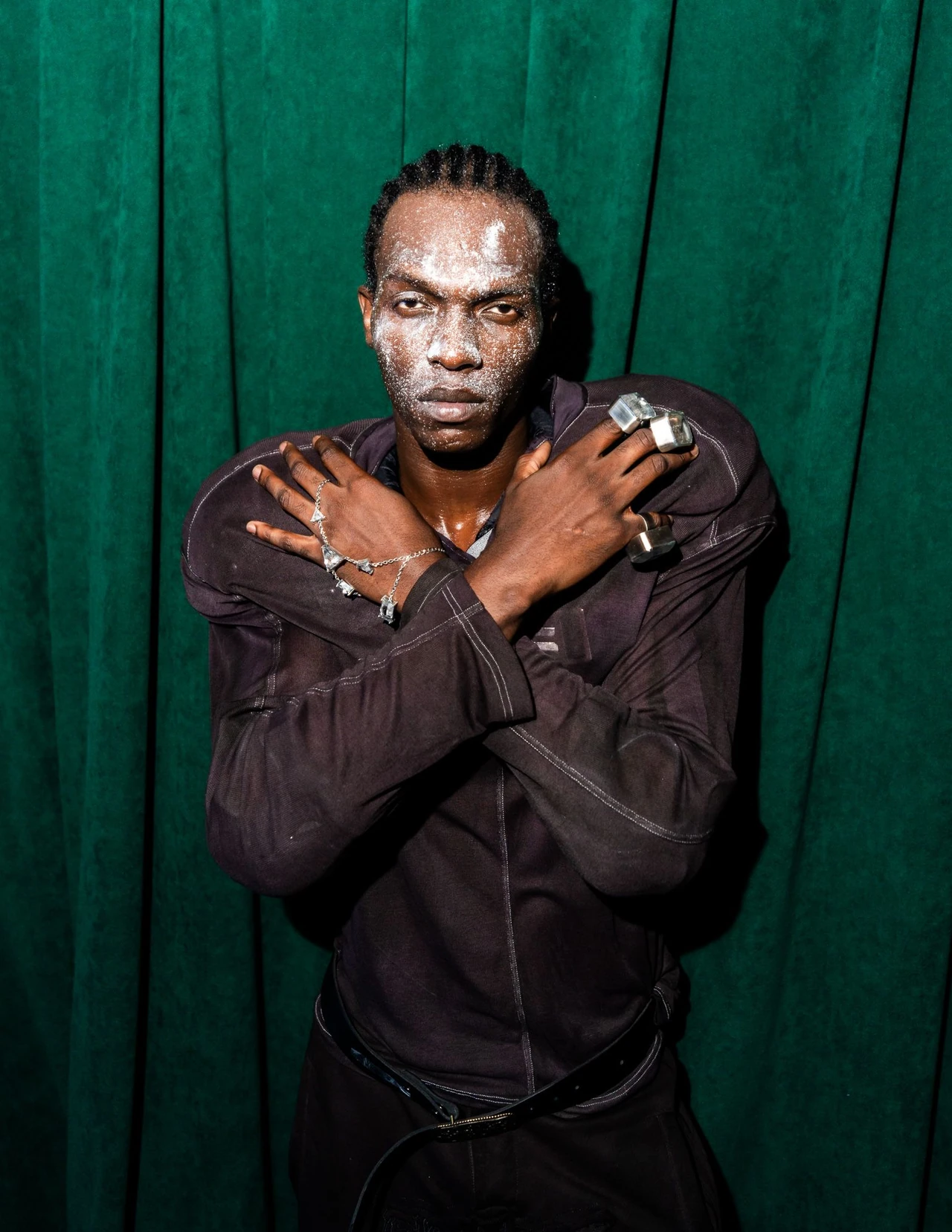 Close portrait of a model with hands crossed at the shoulders against green curtains.