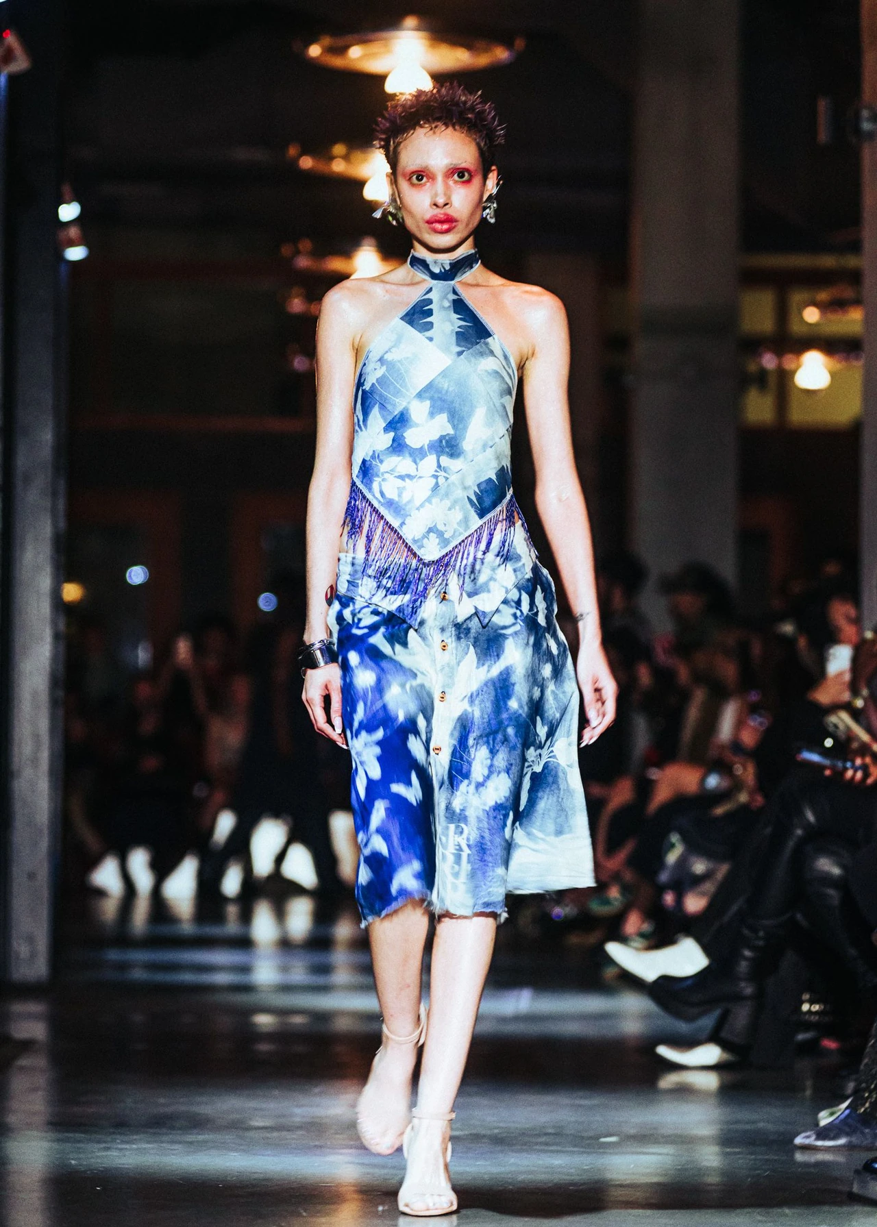 Model wearing a blue-and-white printed halter look beneath warm circular lights.