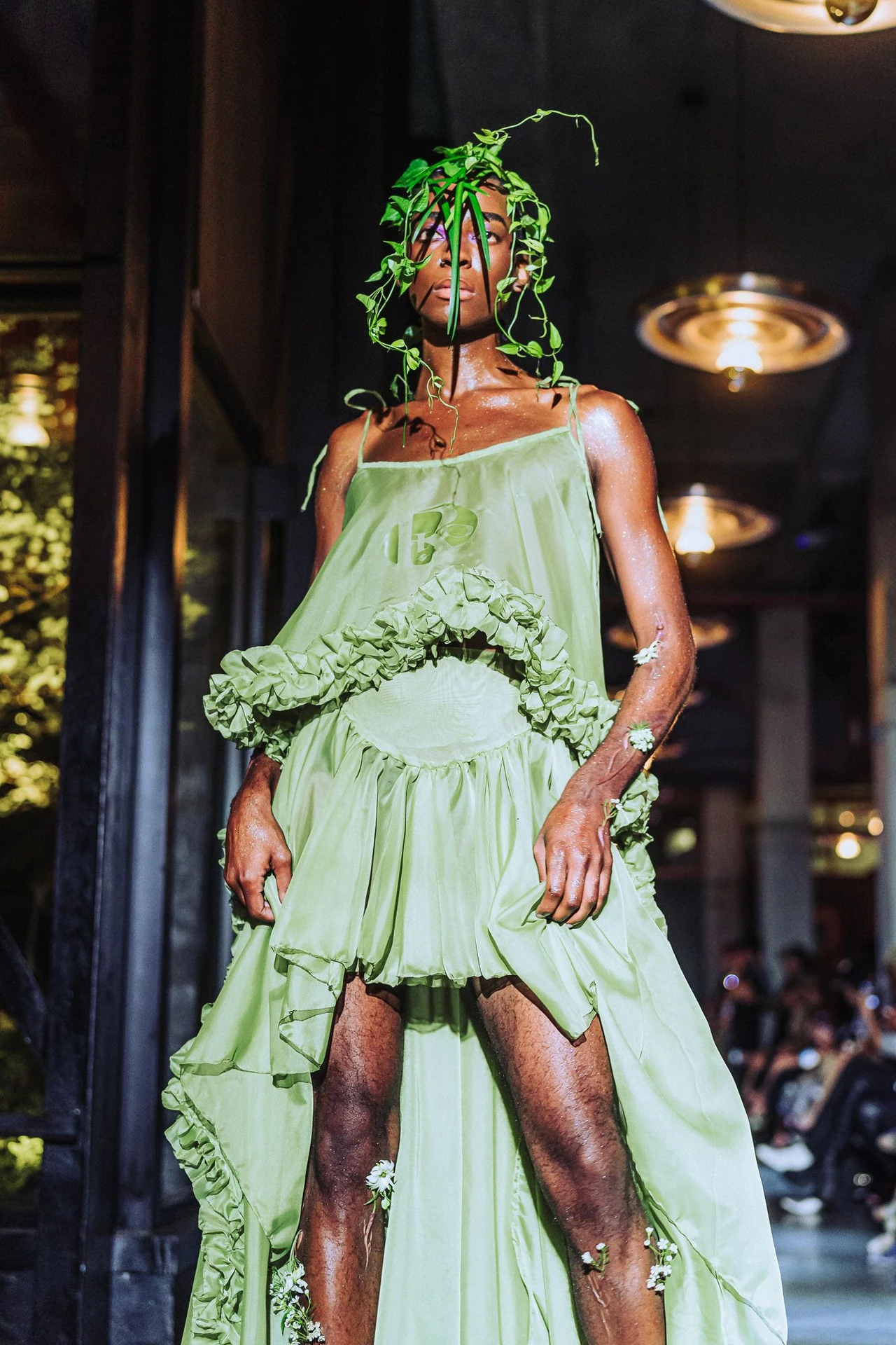 Model wearing a pale green dress with a large sculptural botanical detail.