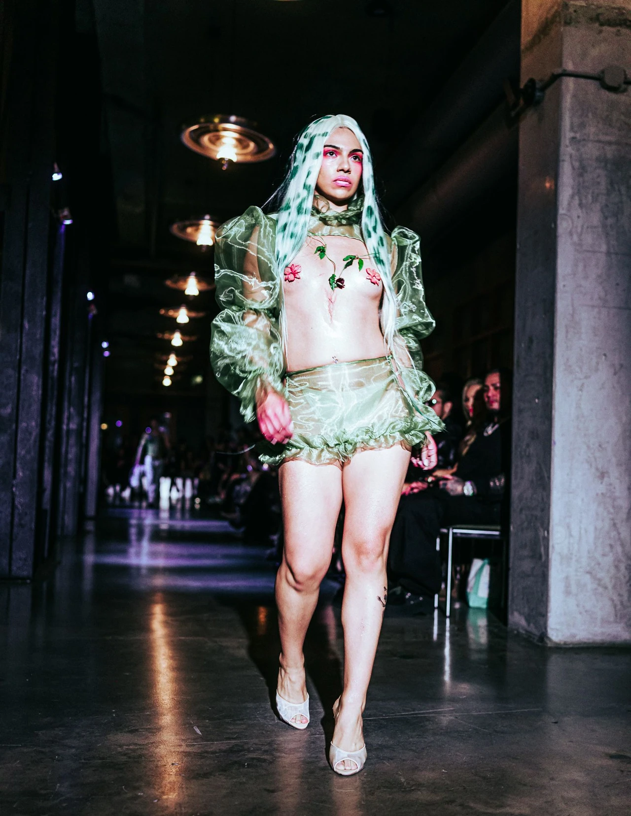 Model in a pale green hooded look with pink accents walking toward the camera.