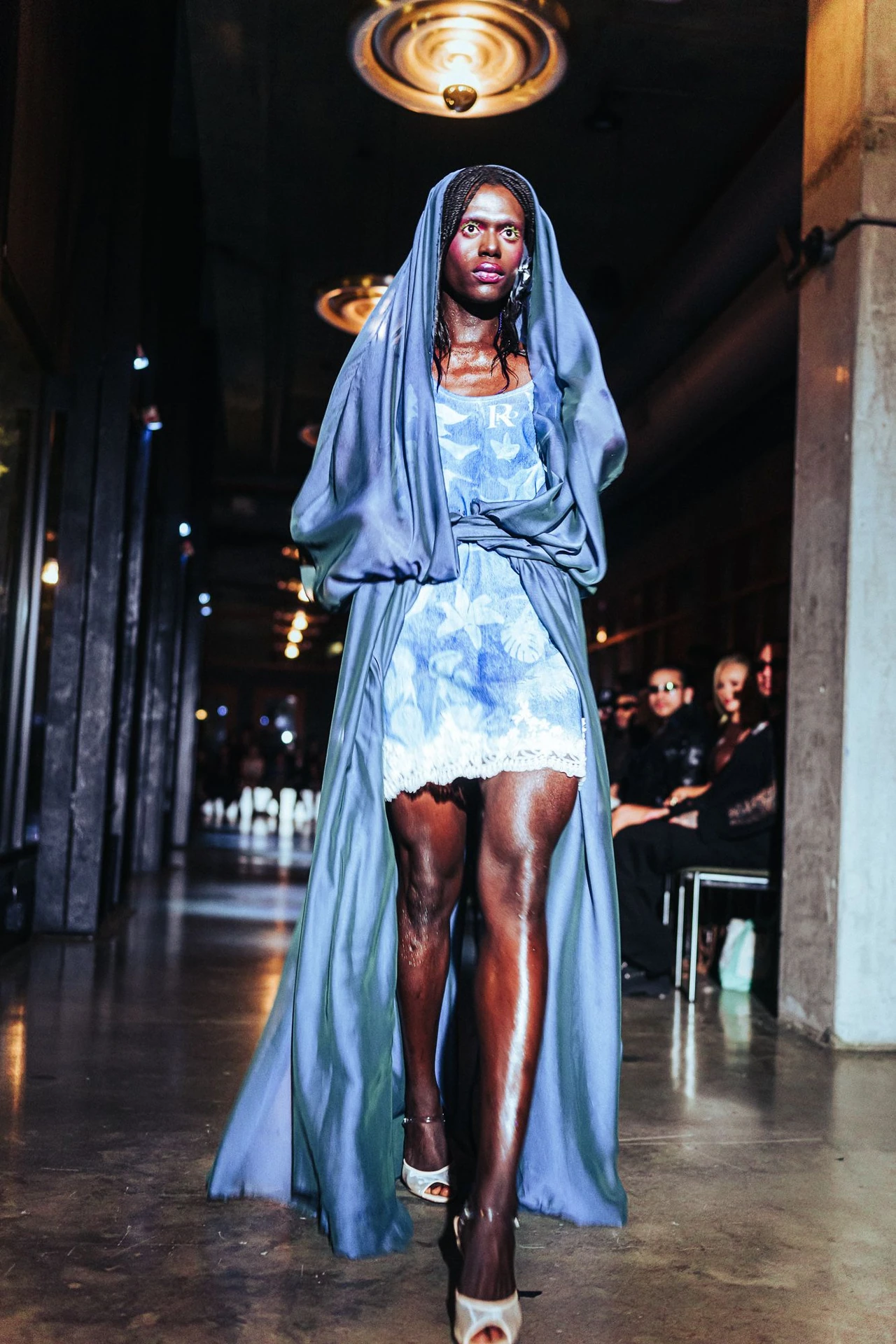 Model in a light blue hooded satin outfit and white shorts on the runway.