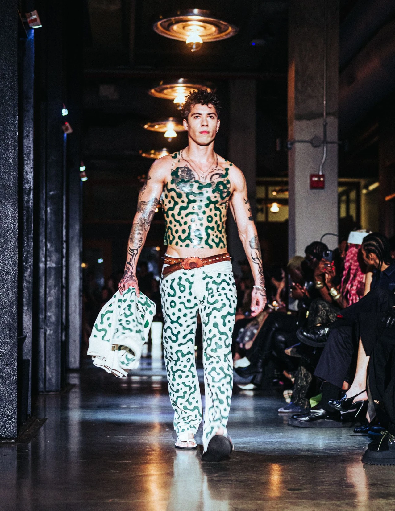 Model in a spotted crop top and loose spotted trousers carrying a matching handbag.