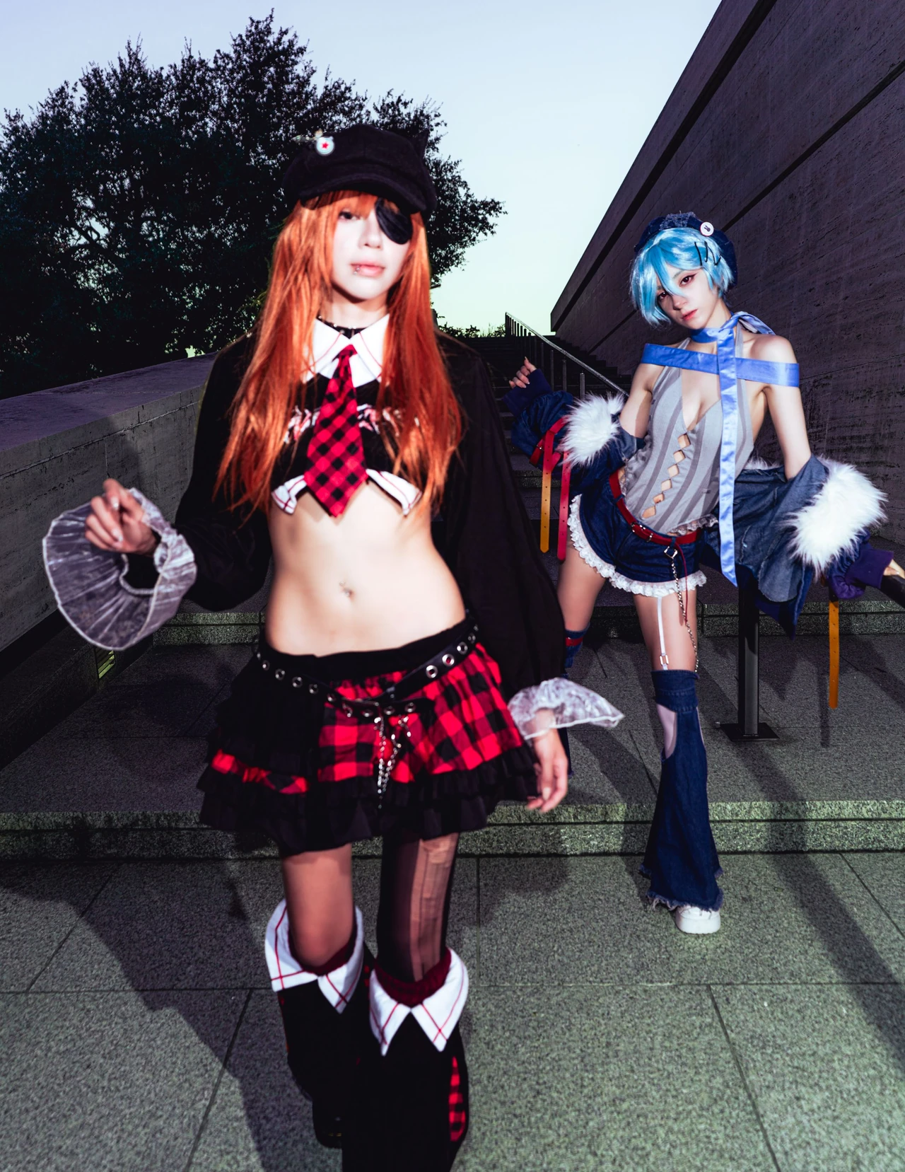 Asuka cosplay in the foreground with Rei standing behind beside a concrete staircase.