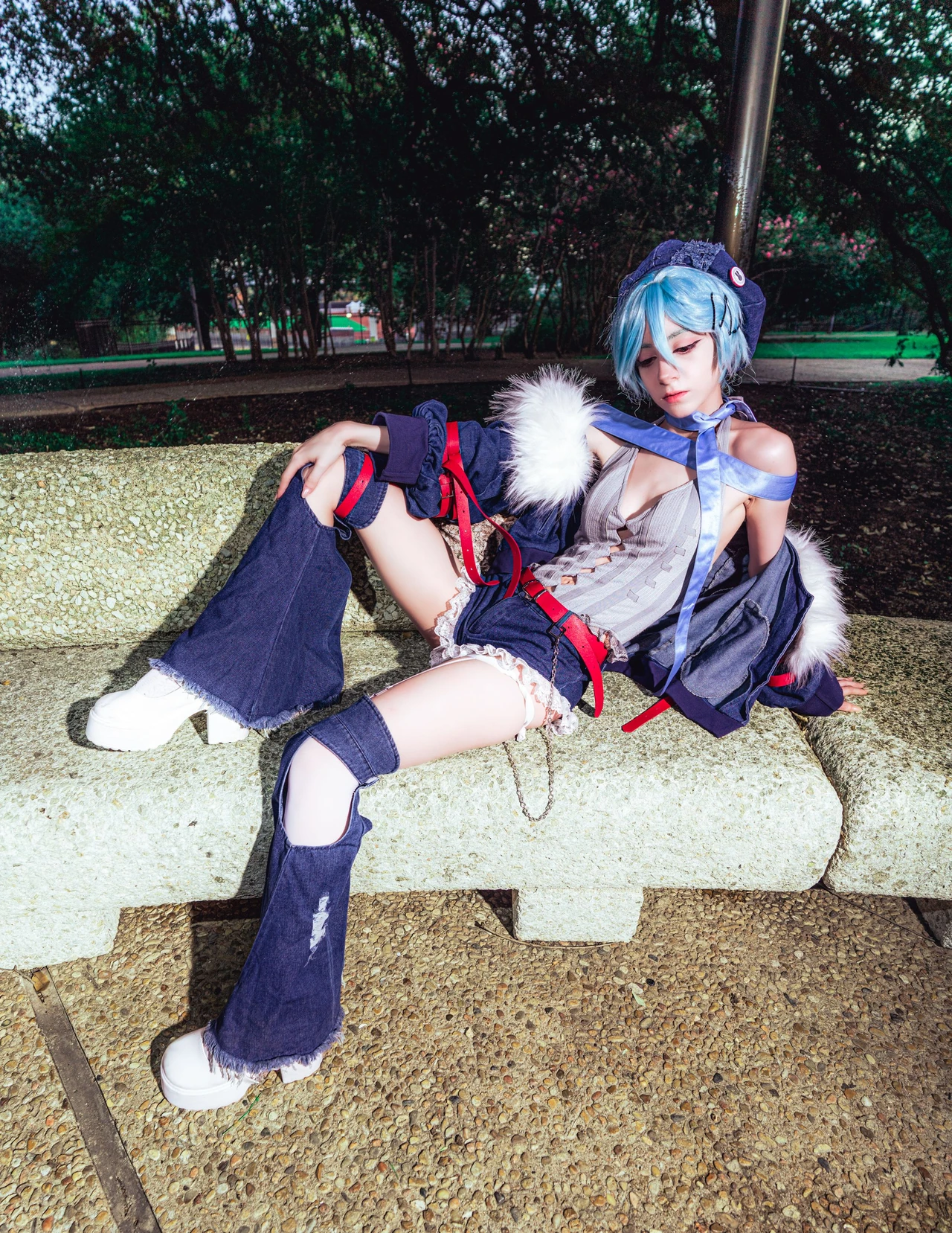 Rei cosplay reclining on a pale concrete bench in a blue cropped jacket and flared trousers.