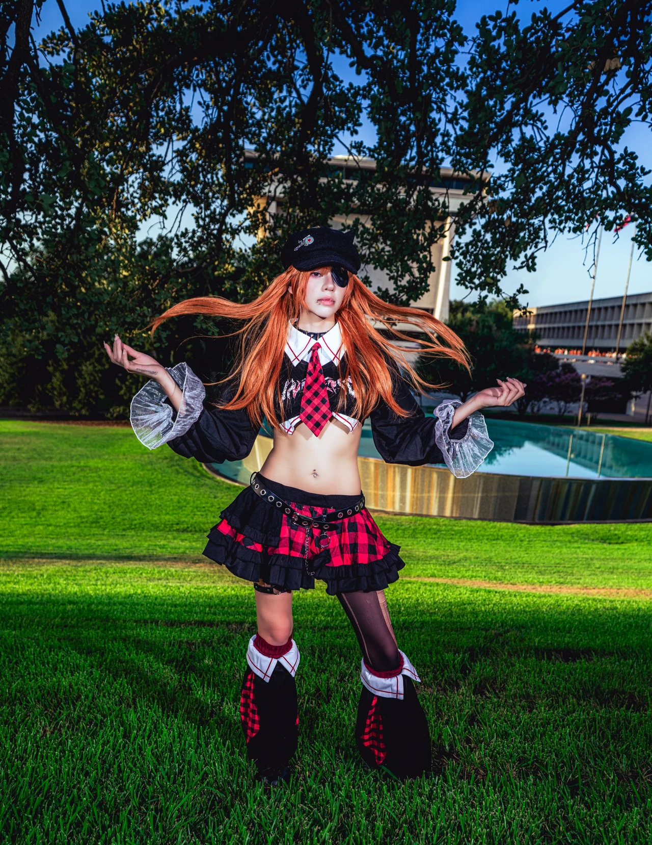 Asuka cosplay in a red plaid skirt with both arms raised against green trees and a blue sky.