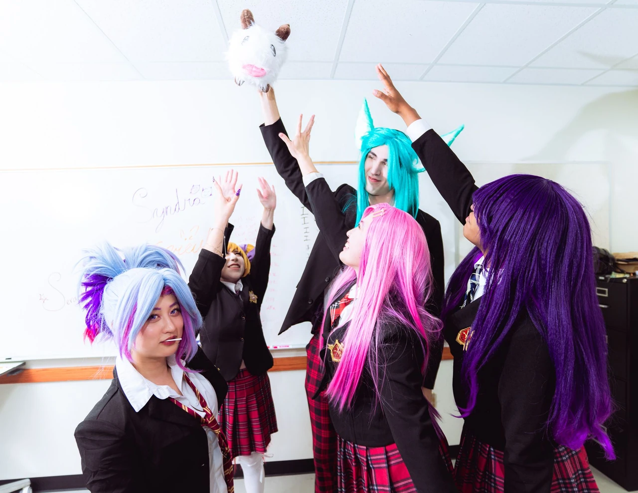 Cosplayers raising their hands toward a small plush toy in the classroom.