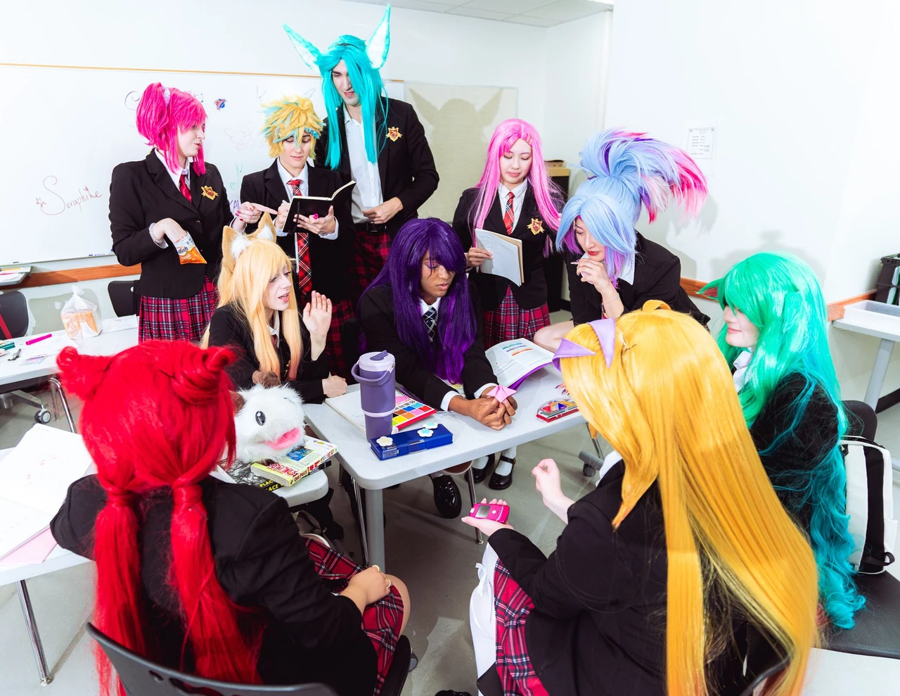 Group of Star Guardian Academy cosplayers gathered around a classroom desk covered in papers.
