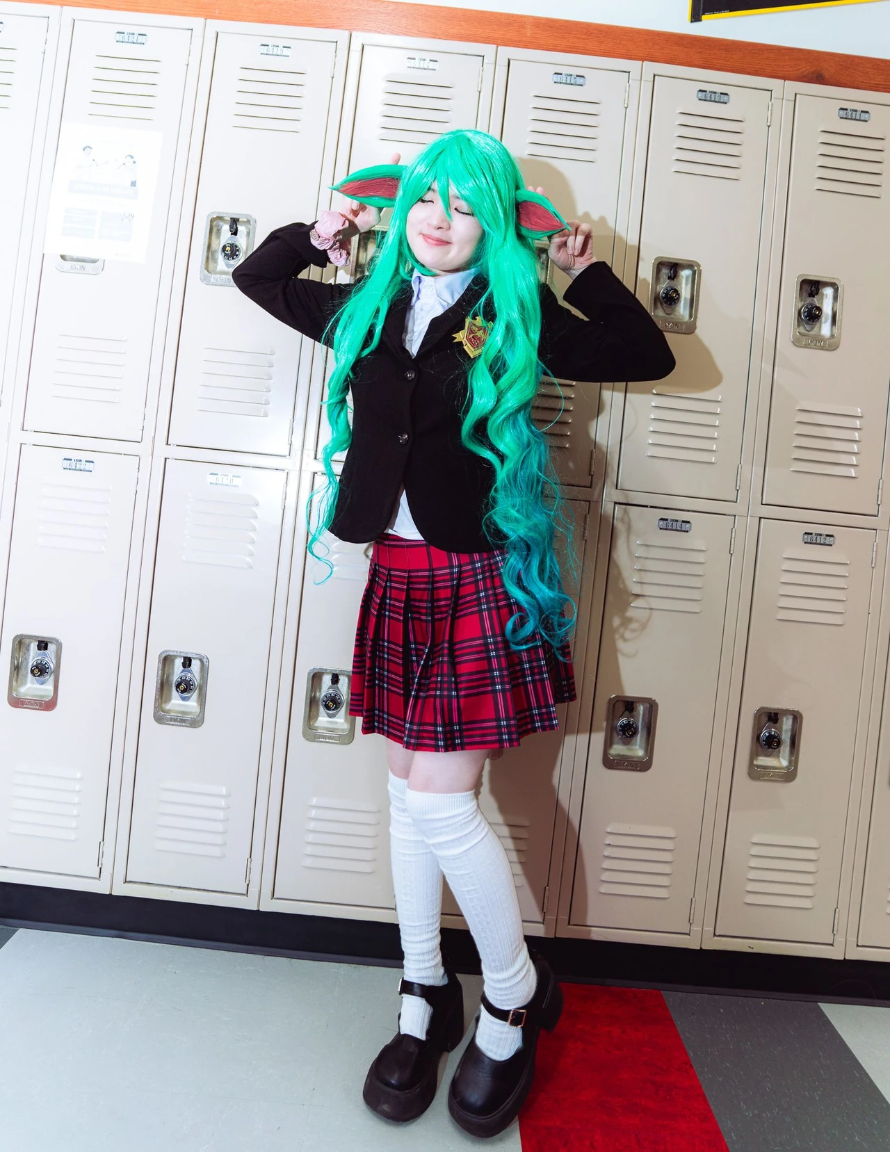Green-haired cosplayer with a horn and pointed ears posing beside cream-colored lockers.
