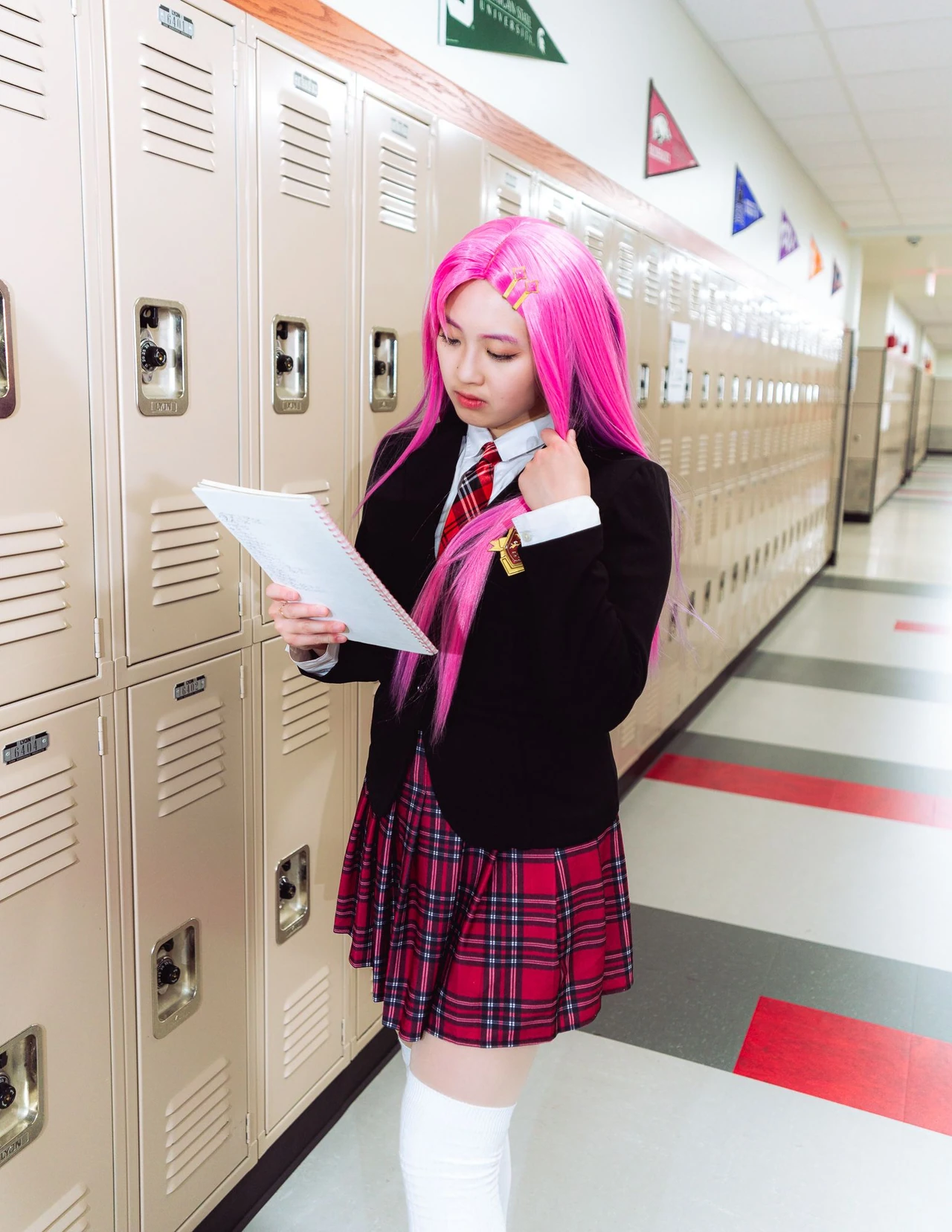 Pink-haired cosplayer reading a sheet of paper beside the lockers.