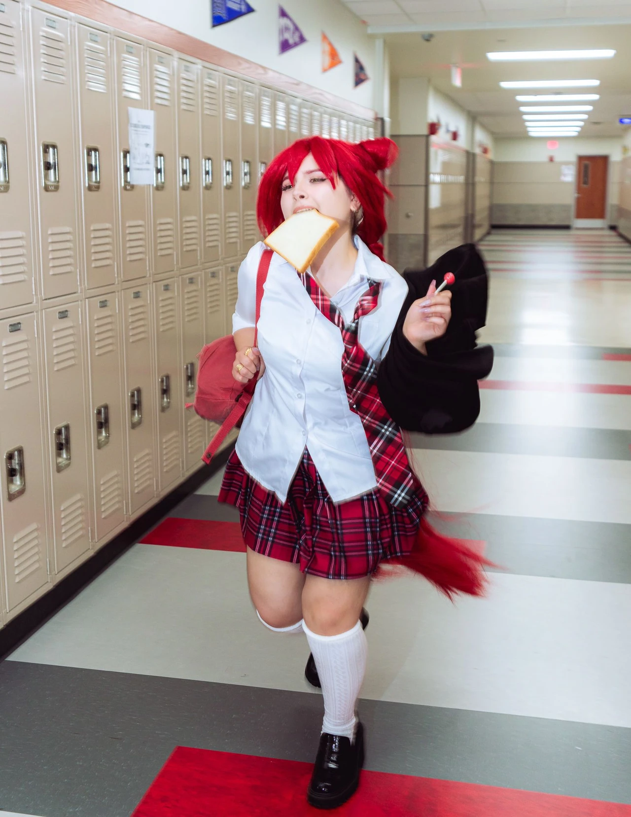 Red-haired cosplayer in an open school blazer holding a lollipop in a corridor.