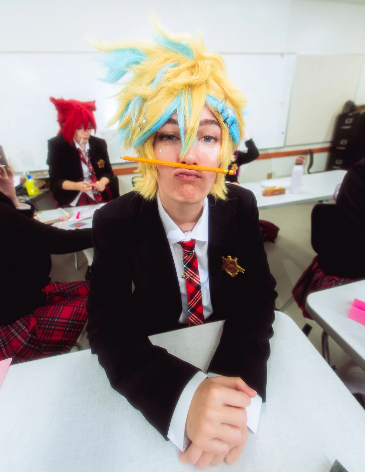 Cosplayer with spiky yellow-and-blue hair balancing a pencil across the face at a desk.