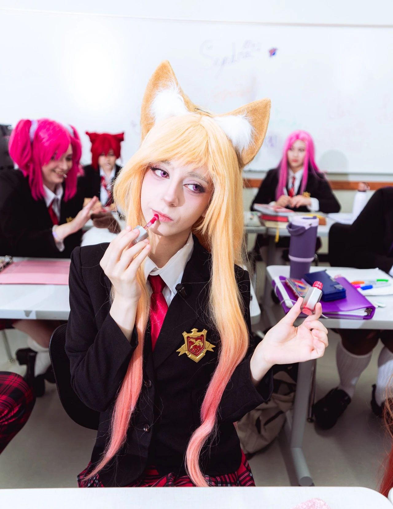 Cosplayer with golden fox ears applying lipstick while classmates sit behind.