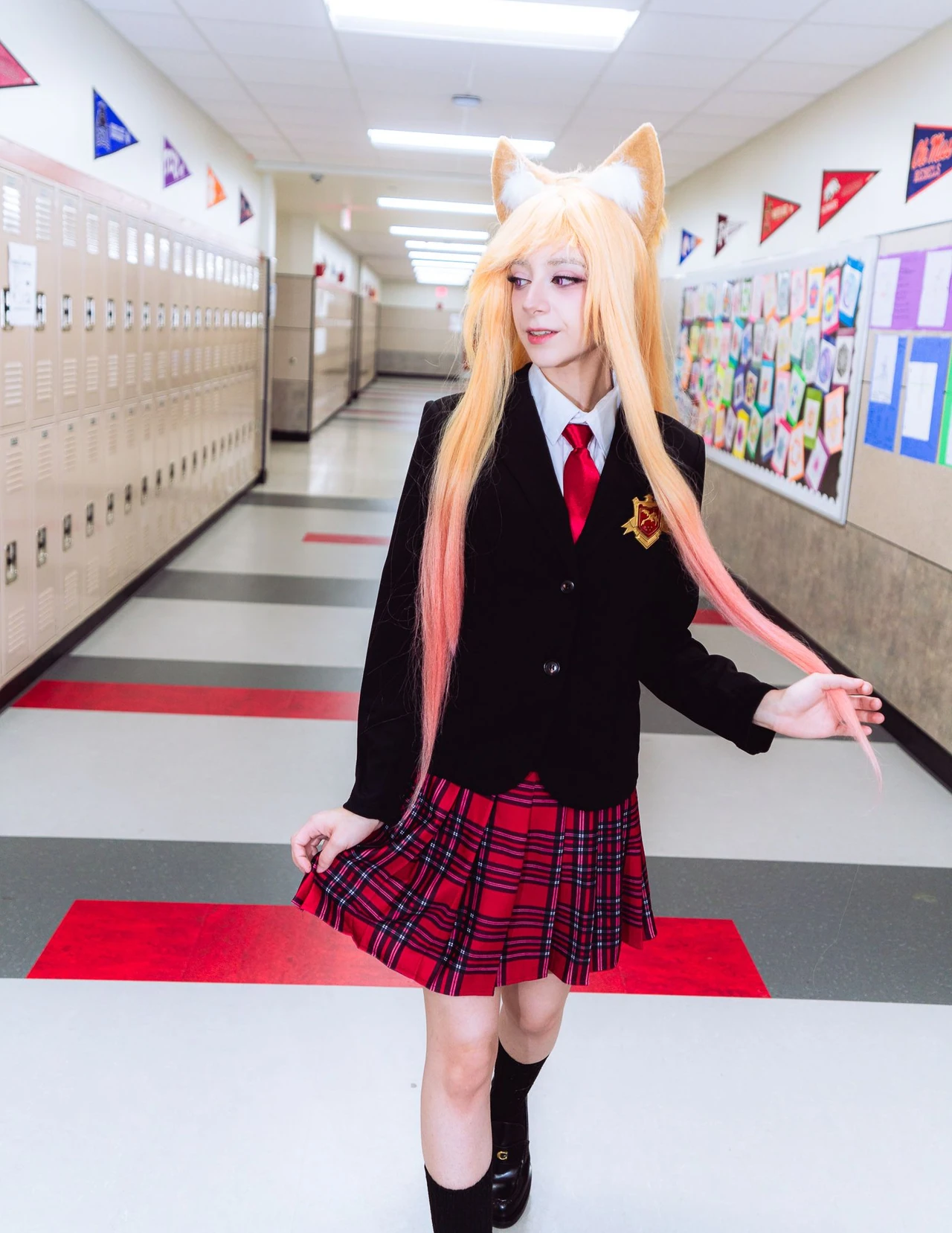Golden-haired cosplayer with fox ears in a black cardigan and plaid skirt in a school hallway.