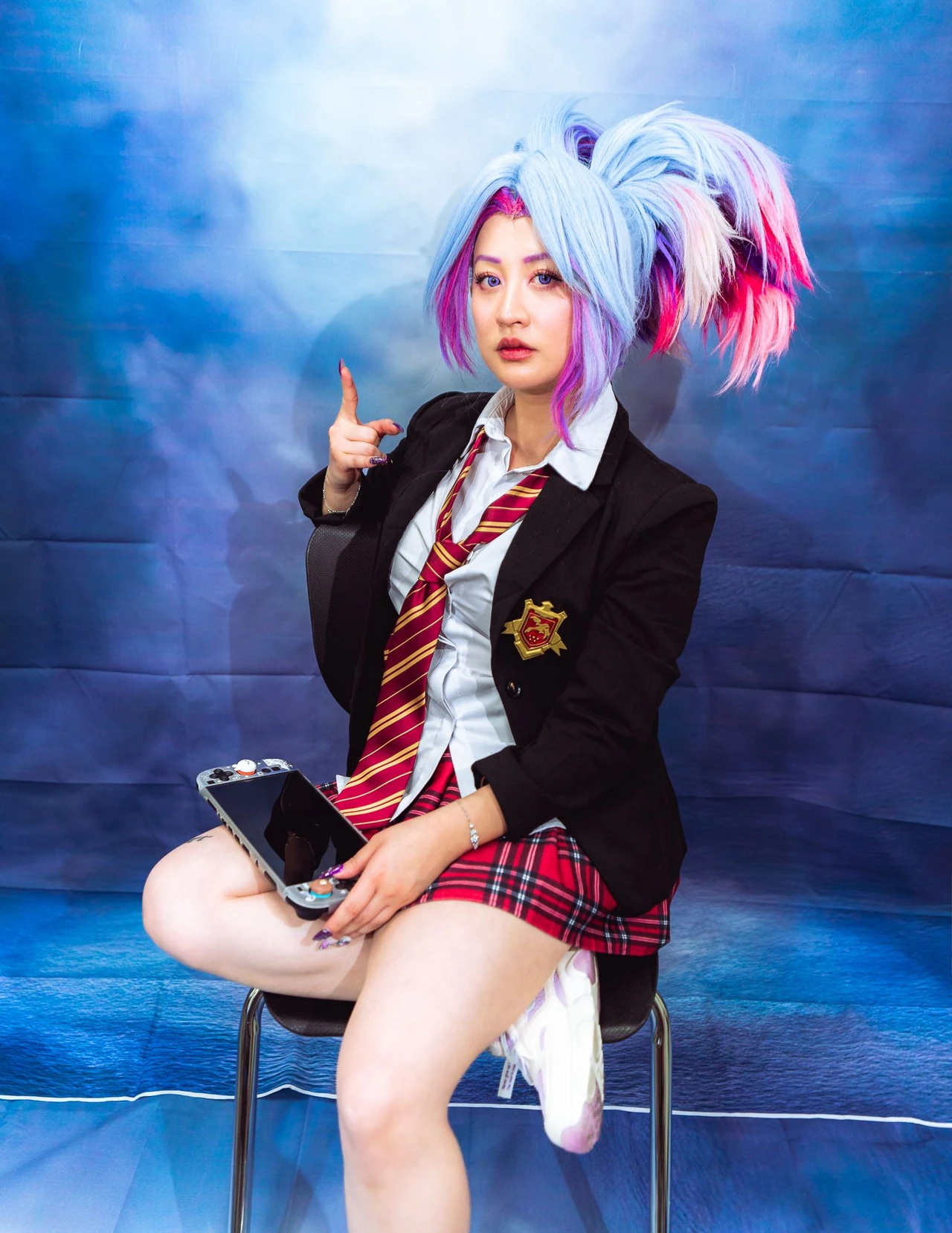 Blue-and-pink-haired cosplayer seated against a blue yearbook-style portrait backdrop.