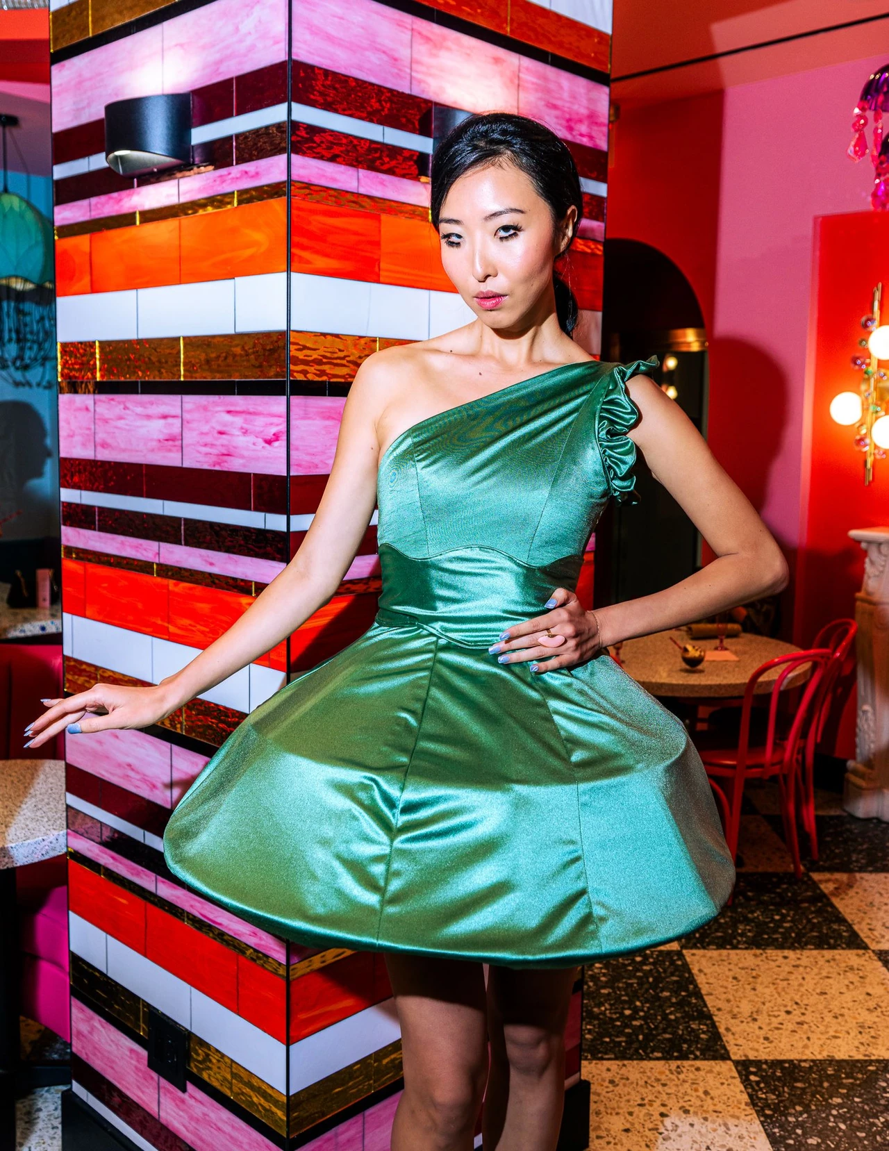 Model in a green one-shoulder bubble dress beside a striped pillar.