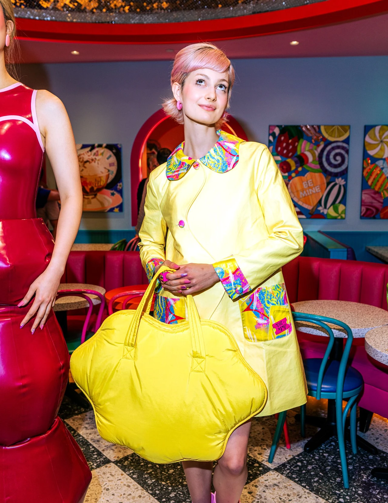 Model wearing a yellow raincoat with a multicolored collar and carrying a sculptural yellow handbag.