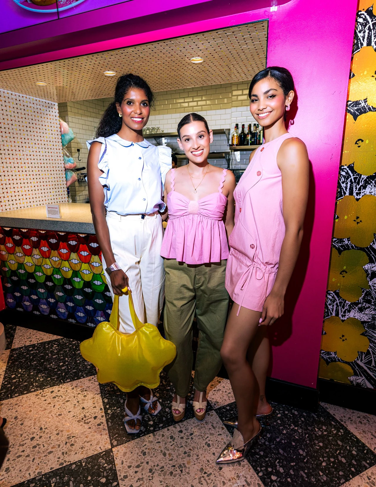 Three models in pastel pink and blue with a yellow sculptural handbag inside Serendipity 3.