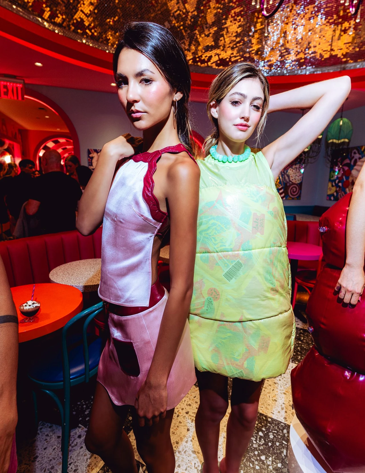 Two models pose in pale yellow and pink outfits with one arm raised.
