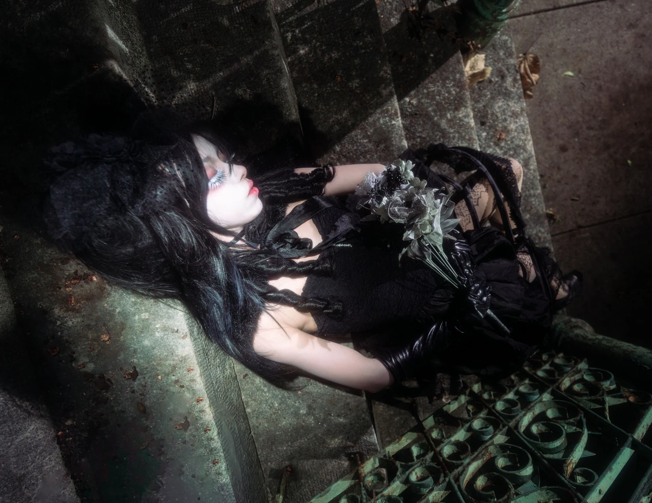 Model in a black dress reclining on a stone step with pale flowers resting at the waist.