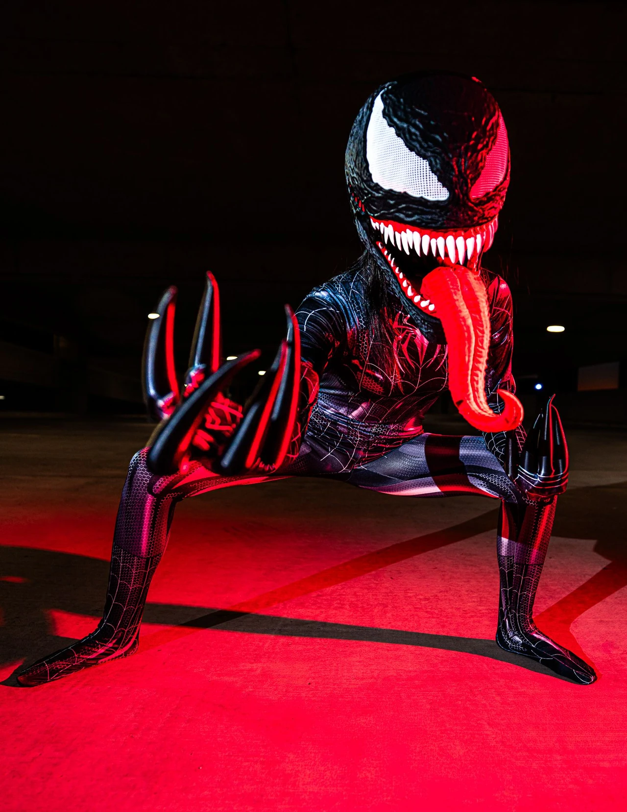 Venom cosplayer crouching on red-lit concrete with an arm extended across the frame.