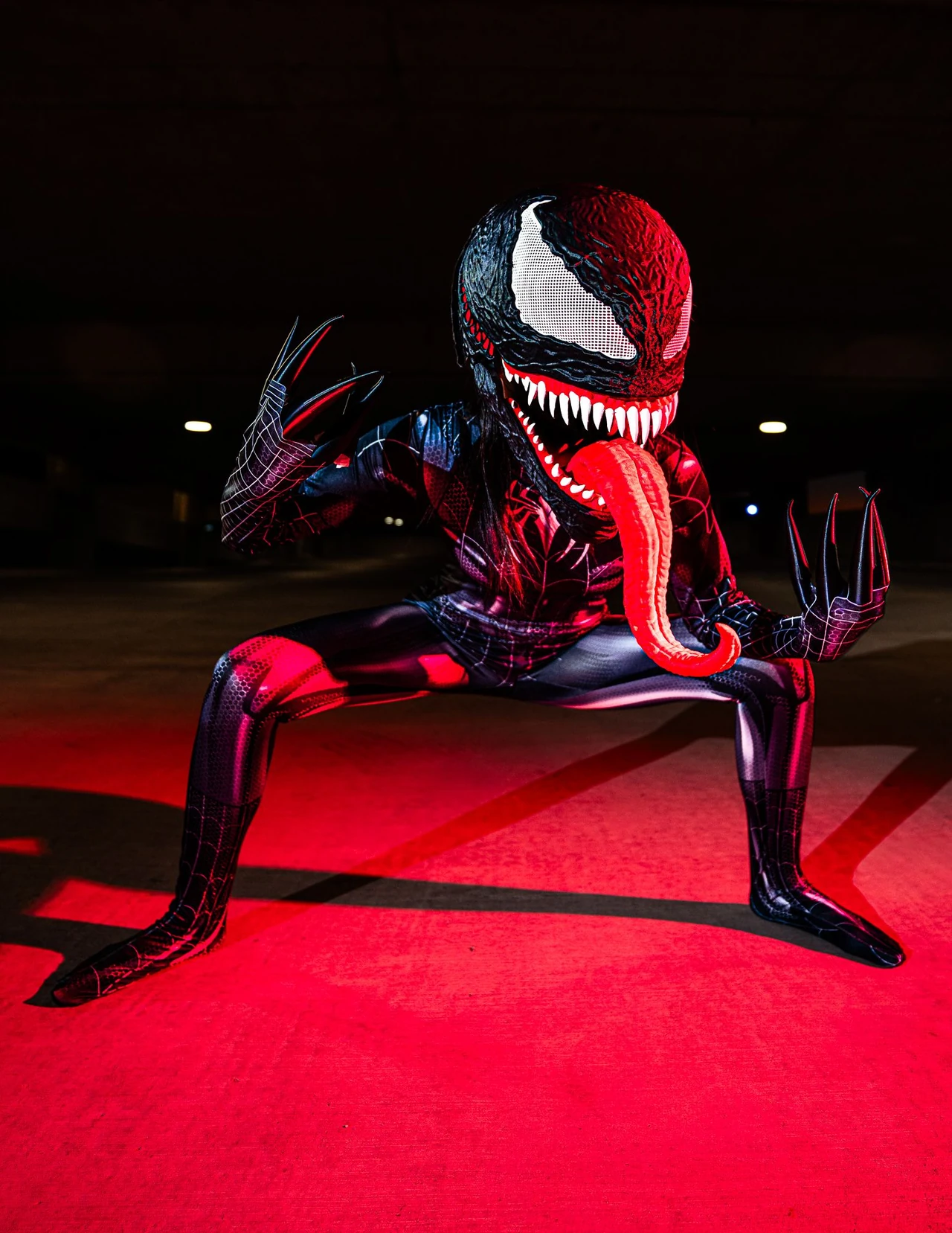 Venom cosplayer leaning into a wide stance with one hand raised and a long red tongue.