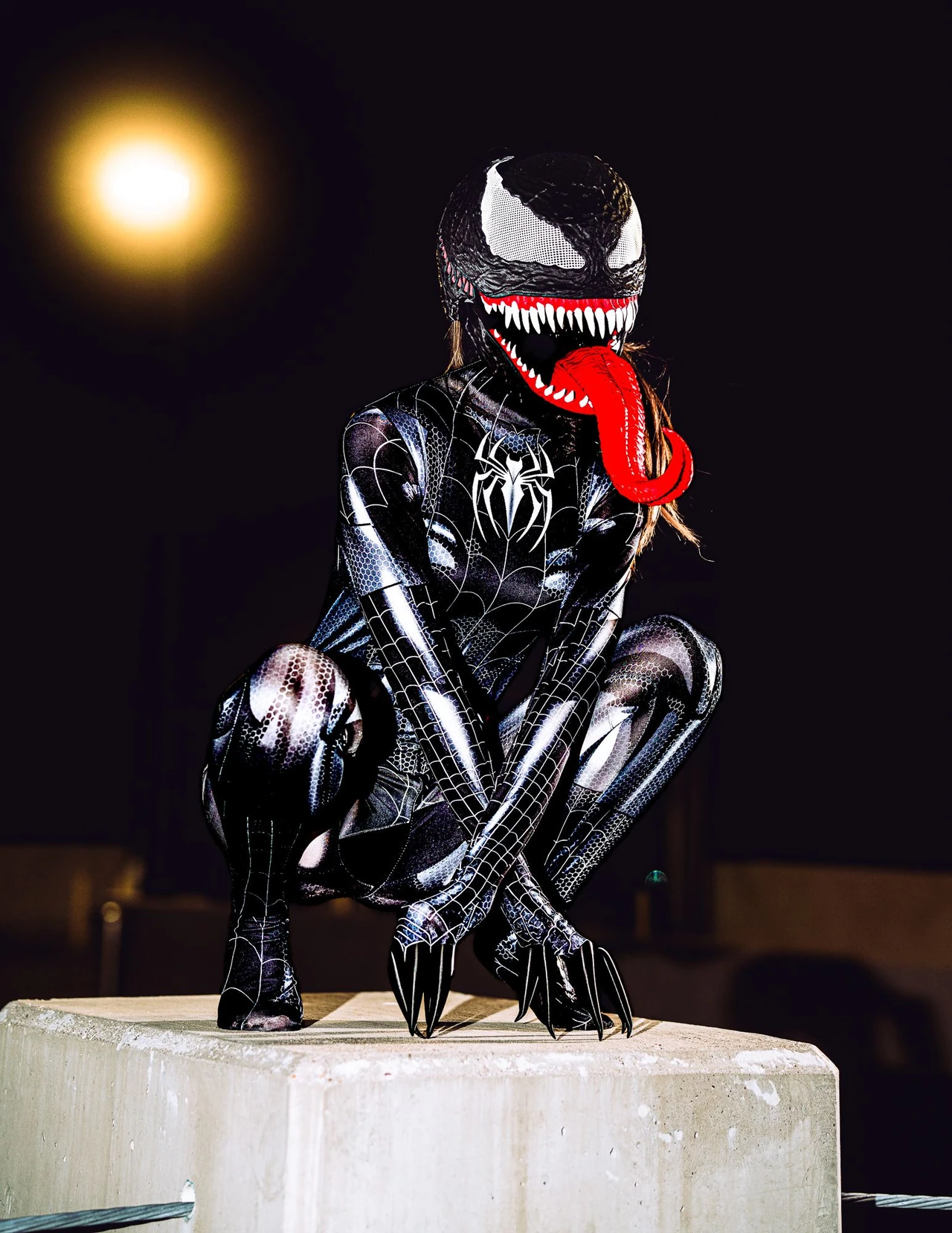 Venom cosplayer crouching on a concrete column beneath a glowing parking-garage light.
