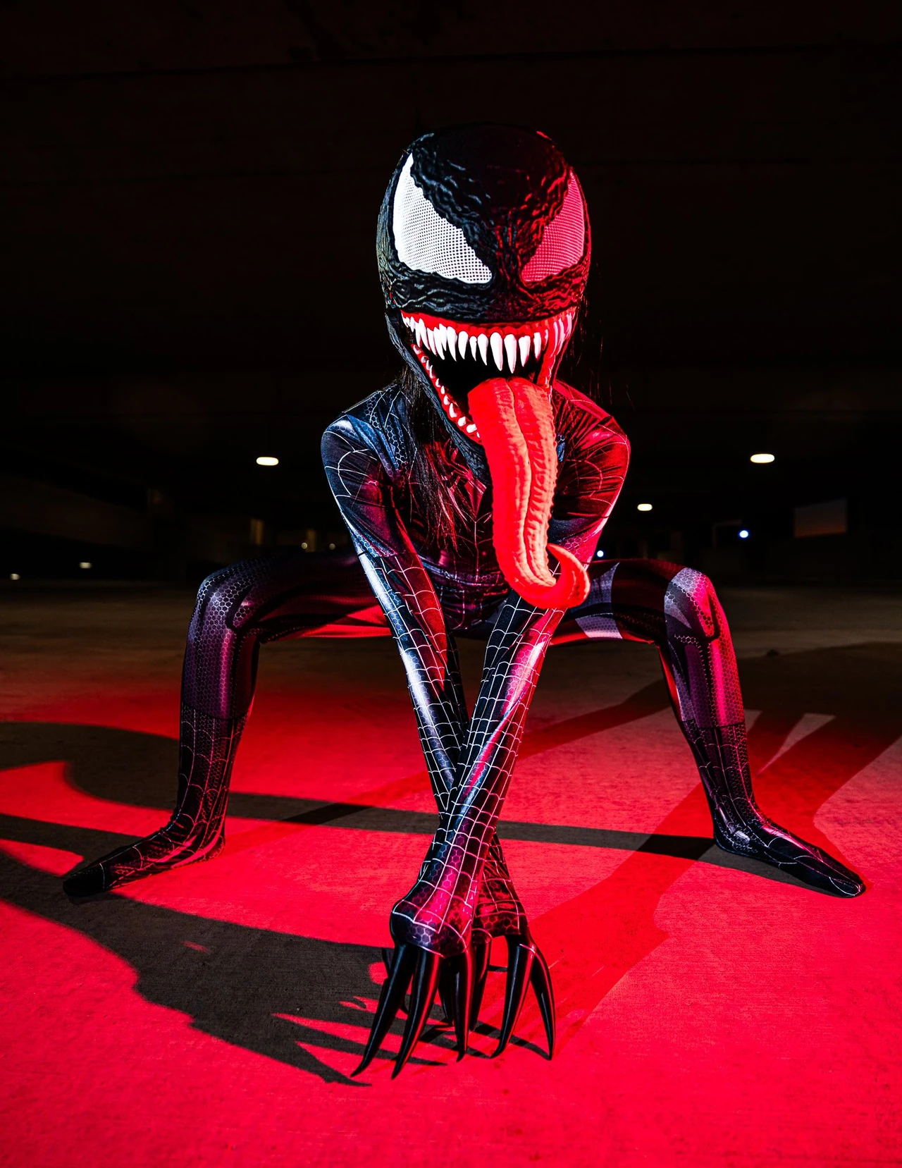 Low-angle portrait of Venom cosplay crouching with a clawed hand spread toward the camera.